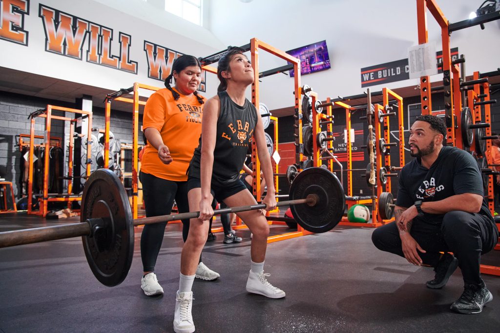 lifting weights in a gym while wearing Sport-Tek ST340, a moisture-wicking performance tee