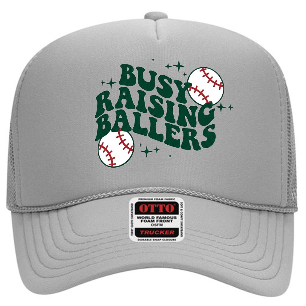 Gray 5-panel mid-profile mesh back trucker hat (32-467) with “Busy Raising Ballers” in bold green text, featuring baseball and star graphics, plus an Otto brand label on the brim.