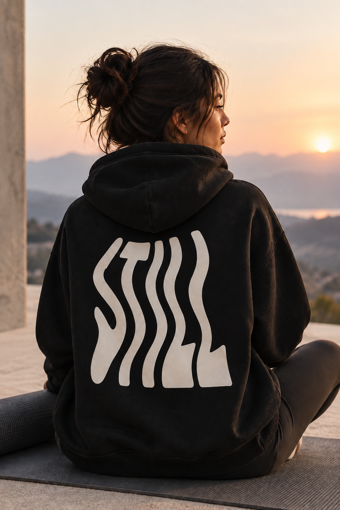 Woman wearing an AS Colour Men's Relax Zip hoodie with minimalist yoga-inspired artwork while meditating outdoors